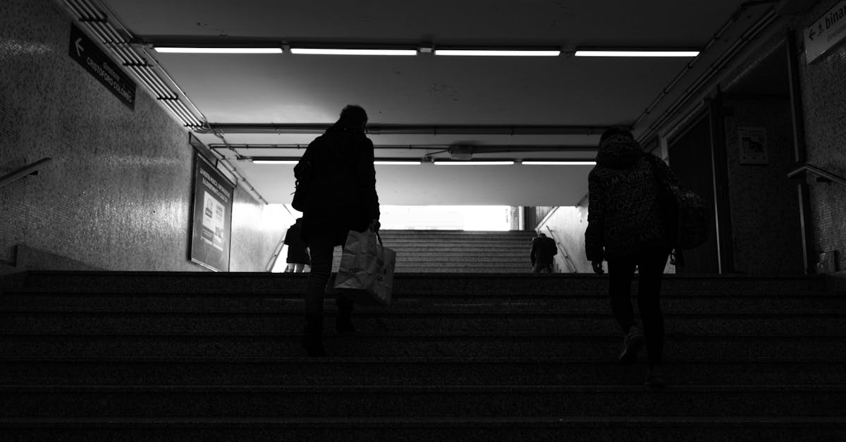 Vue arrière en noir et blanc de passagers anonymes montant un escalier pour sortir de la station de métro.