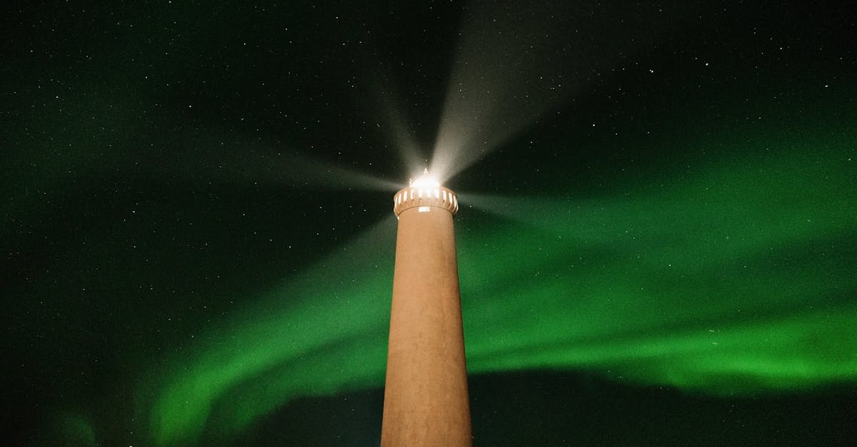 De en dessous de la haute tour de phare brûlant dans la nuit sombre contre le ciel noir avec une lueur verte brillante de l'aurore boréale dans le nord.