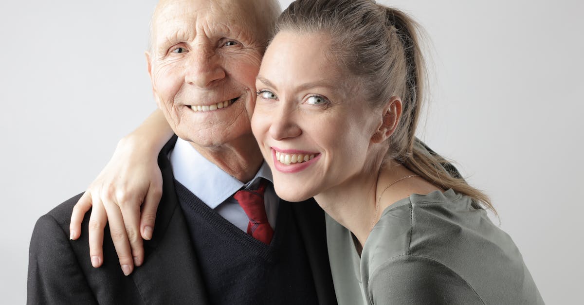 Un homme âgé joyeux et une femme adulte câlinant sur un fond blanc et regardant l'appareil photo.