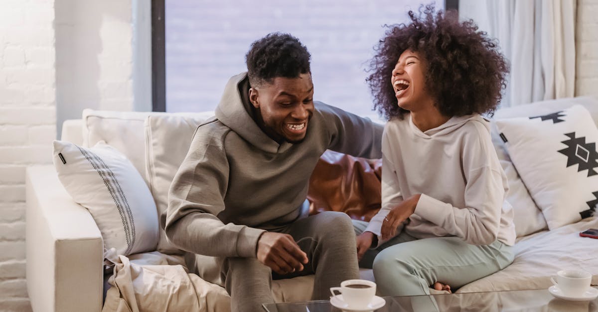 Jeune couple afro-américain joyeux en tenue décontractée riant heureusement ensemble alors qu'ils se reposent sur un canapé confortable à la maison.