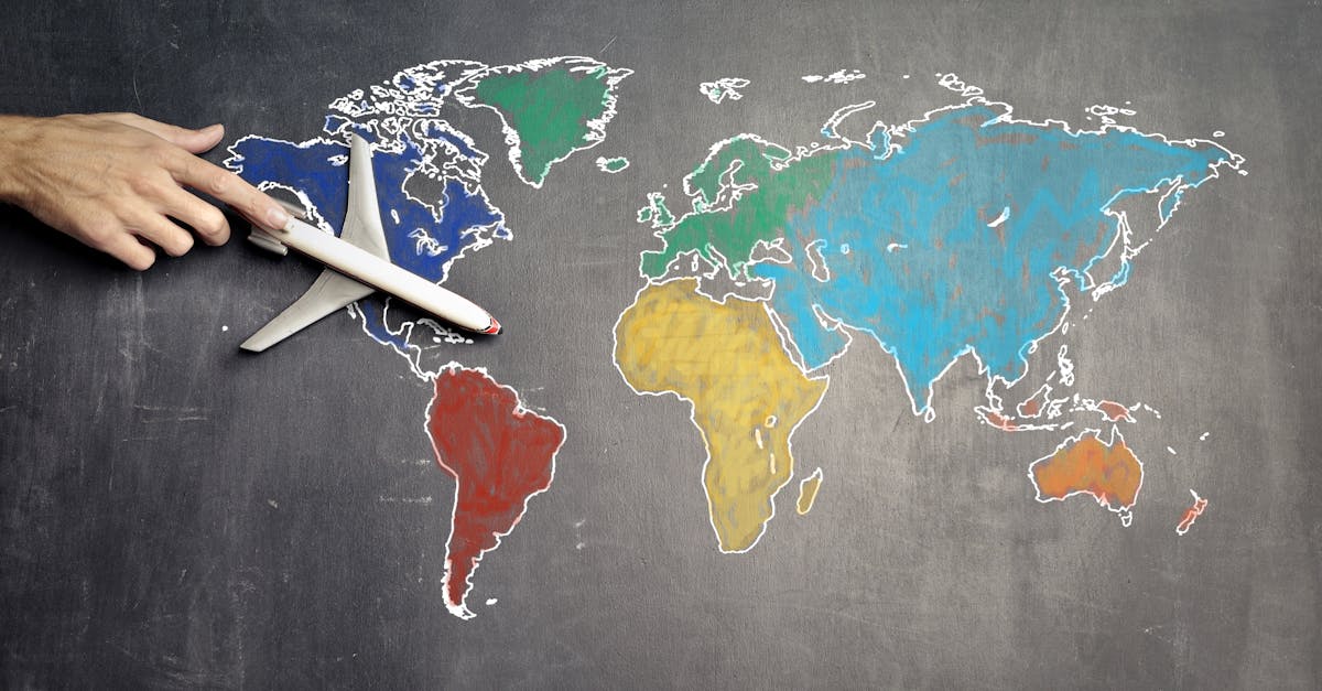 Vue de dessus d'une personne anonyme tenant un avion jouet sur une carte du monde colorée dessinée sur un tableau noir.