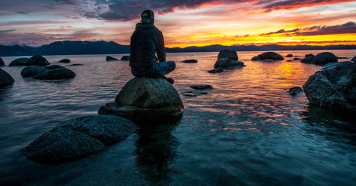 Personne assise sur un rocher au bord de l'eau.