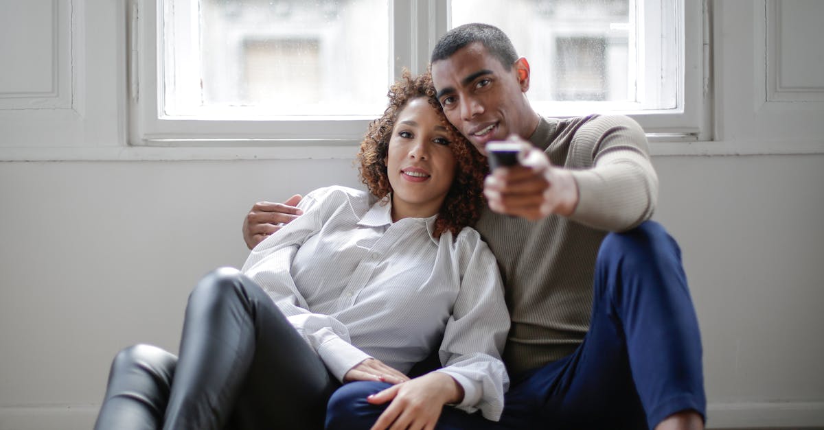 Couple ethnique amoureux regardant un film en s'enlaçant par terre près de la fenêtre.