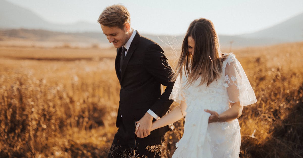 Photo en mise au point peu profonde d'un homme en costume noir tenant la main d'une femme en robe blanche.