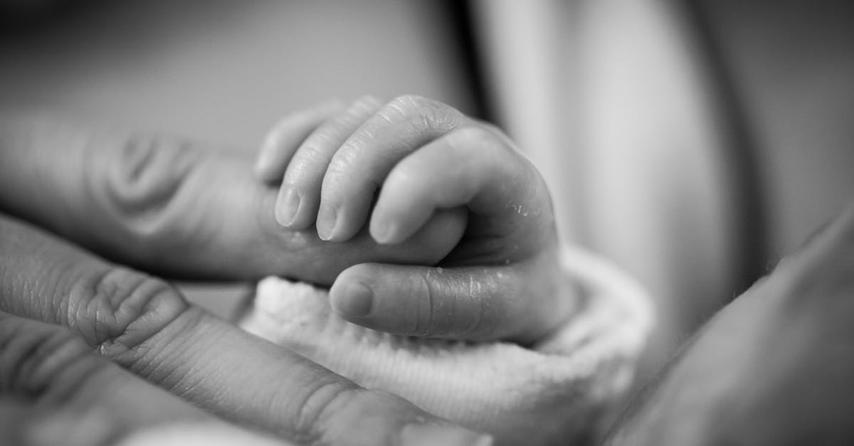 Photographie en niveaux de gris d'un bébé tenant un doigt.