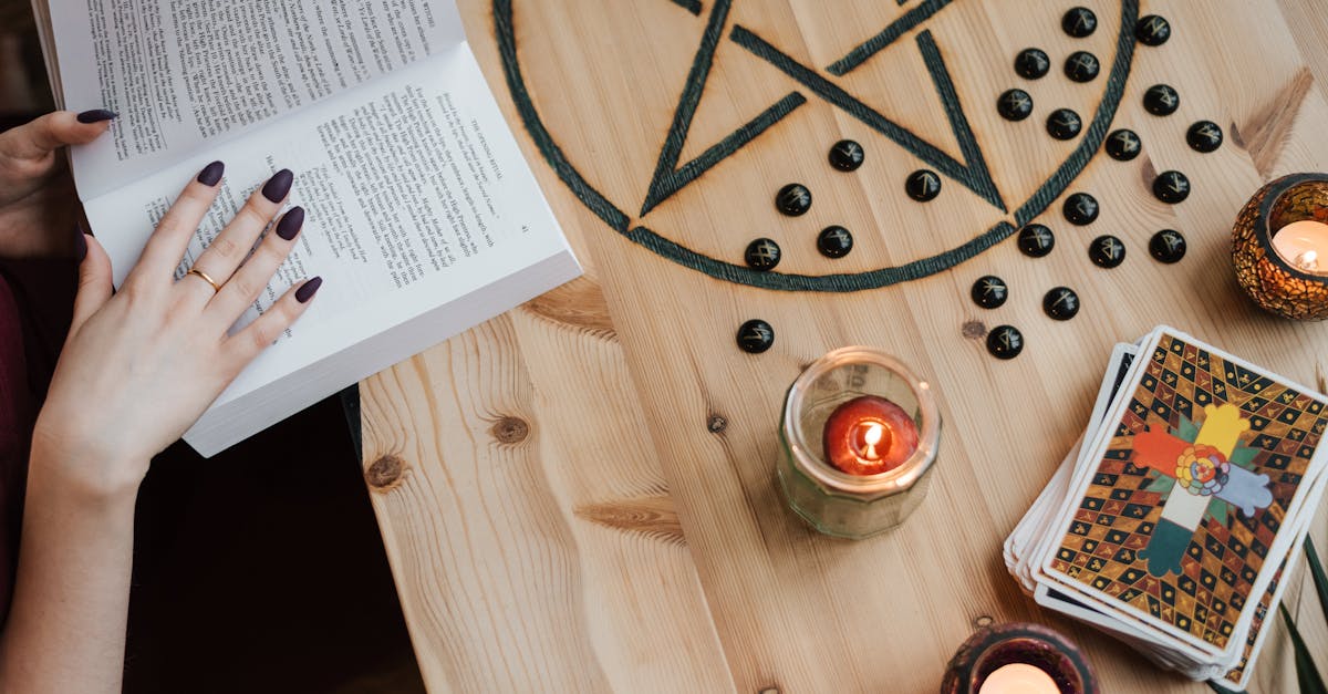 D'une vue aérienne, une diseuse de bonne aventure non reconnaissable est en train de lire un livre à une table avec des cartes de tarot et des bougies pendant un processus de divination.
