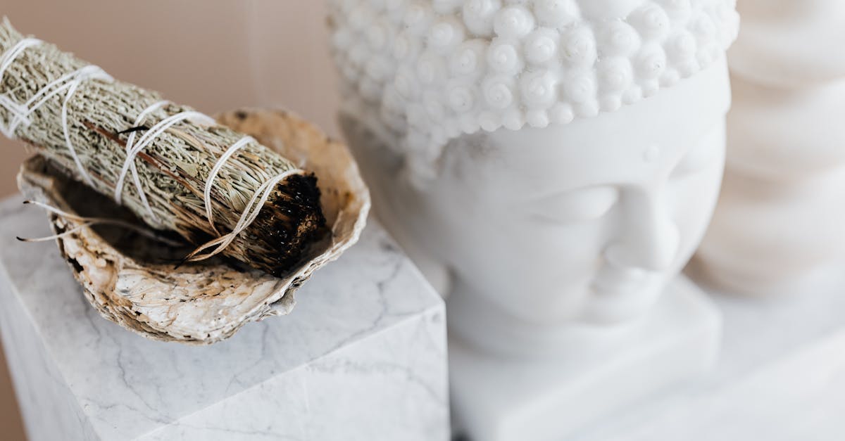 D'une bougie de sauge surplombant un bol placé sur une étagère en marbre blanc près d'un buste de bouddha en plâtre et d'un vase de forme créative pour la décoration de la maison.