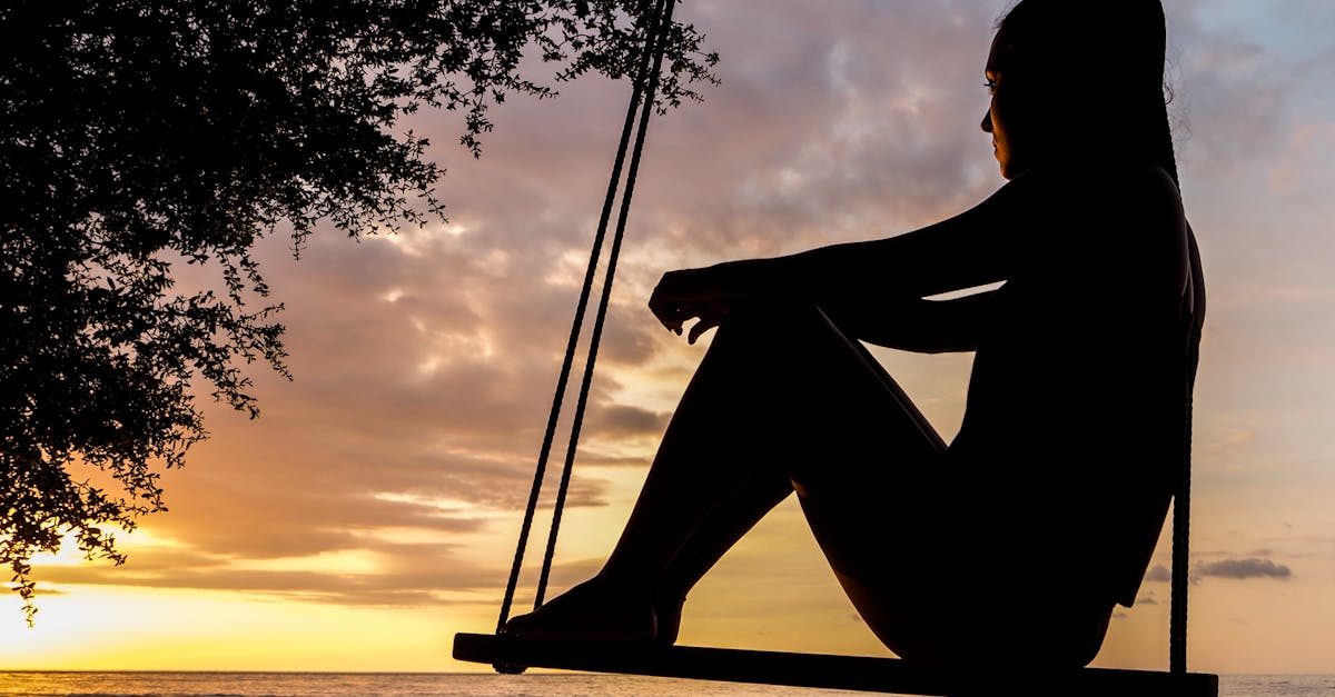 Silhouette d'une femme sur une balançoire lors de l'heure dorée.