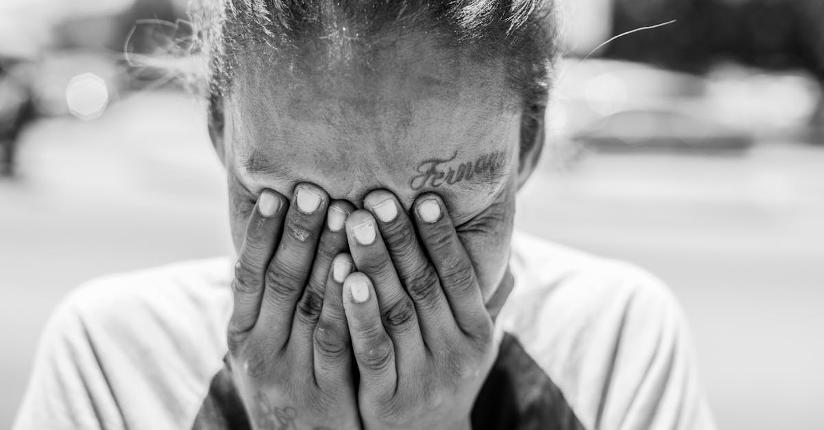 Photo en noir et blanc d'une personne couvrant son visage avec les mains.