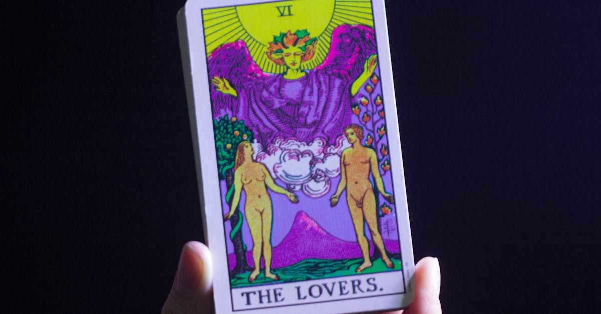 Une personne non reconnaissable, une diseuse de bonne aventure, démontrant la carte de tarot des Amoureux en main tout en effectuant une lecture de cartes sur fond noir dans une pièce.