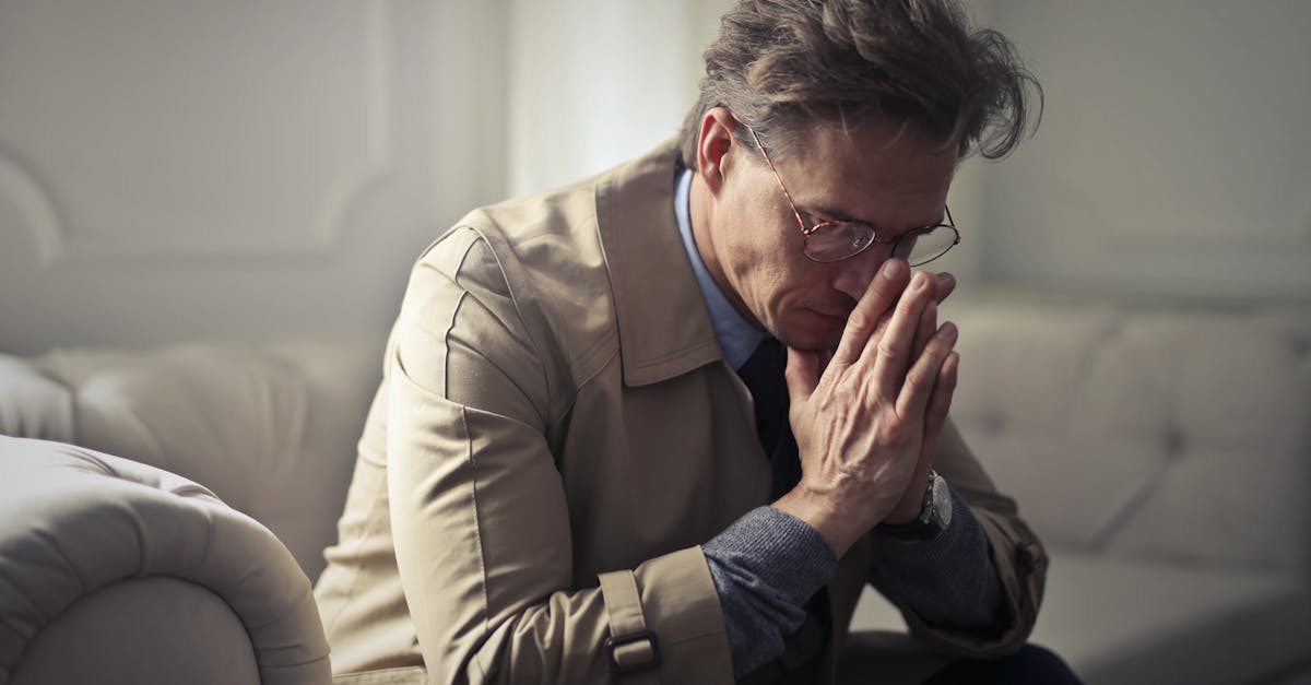 Vue latérale d'un entrepreneur homme contrarié en tenue formelle, assis sur un canapé dans un salon moderne, réfléchissant à ses problèmes financiers, en appuyant sur les mains et en regardant vers le bas.