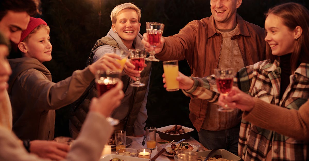 Des amis riant avec leurs enfants passent du temps dans le jardin en soirée, profitant d'un dîner avec des guirlandes et des verres qui s'entrechoquent.
