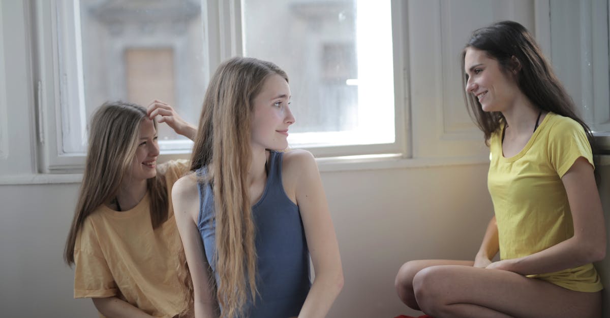 Un groupe de jeunes femmes amicales en culottes et t-shirts se regroupe sur le sol dans une pièce en désordre, échangeant des conversations tout en souriant et en se regardant.