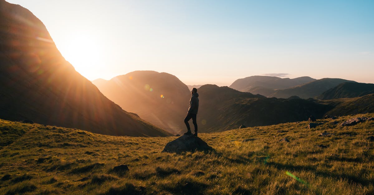 Photographie de silhouette d'une personne debout sur de l'herbe verte devant des montagnes pendant l'heure dorée.
