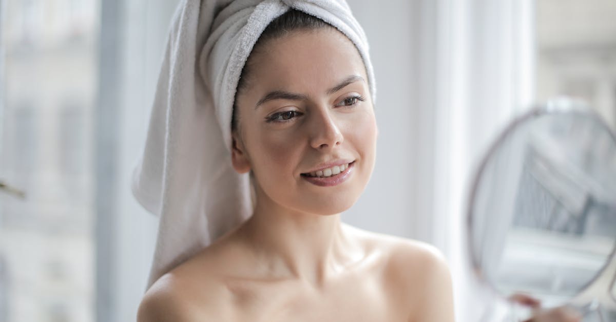 Portrait en plongée d'une femme souriante, les cheveux recouverts d'une serviette, se regardant dans le miroir