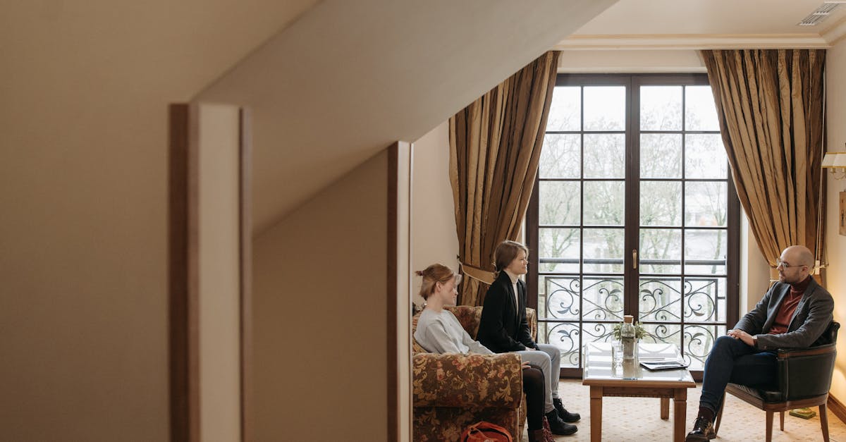 Un homme en manteau gris assis sur une chaise conversant avec une femme installée sur un canapé