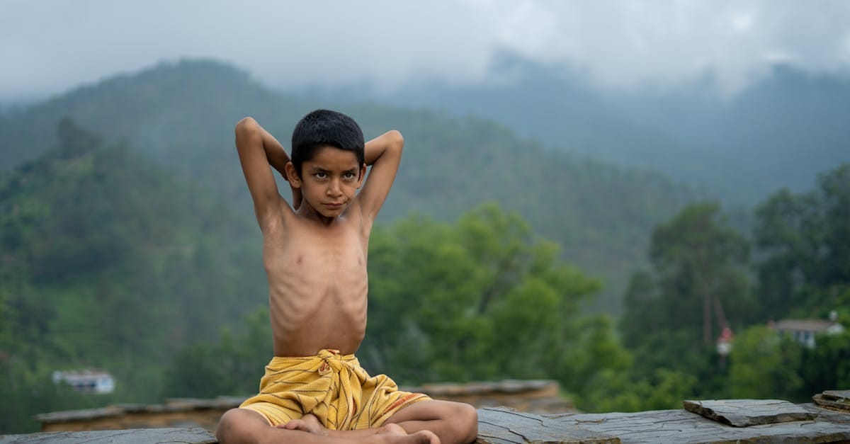 Un jeune garçon en posture de yoga en plein air, entouré de collines verdoyantes, incarnant le bien-être naturel.