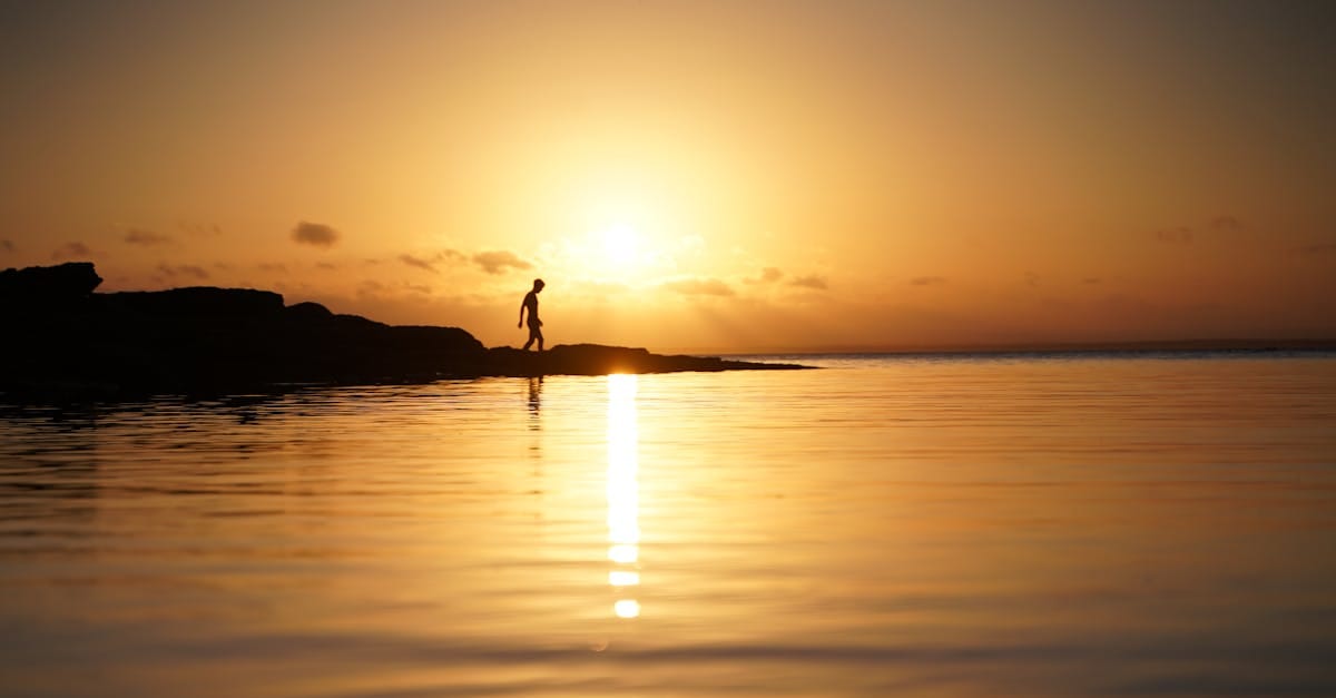 Une silhouette solitaire se promène le long de la plage de Currarong au coucher du soleil, se reflétant sur des eaux sereines.