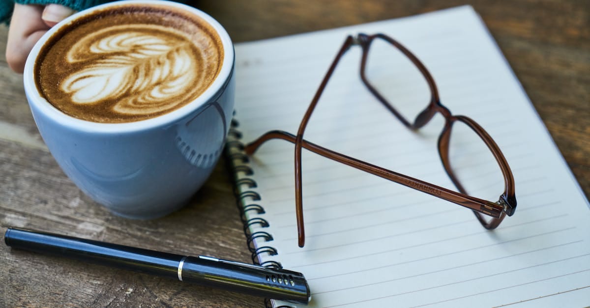 Espace de travail douillet avec un art du latte, un carnet et des lunettes, idéal pour stimuler la créativité.