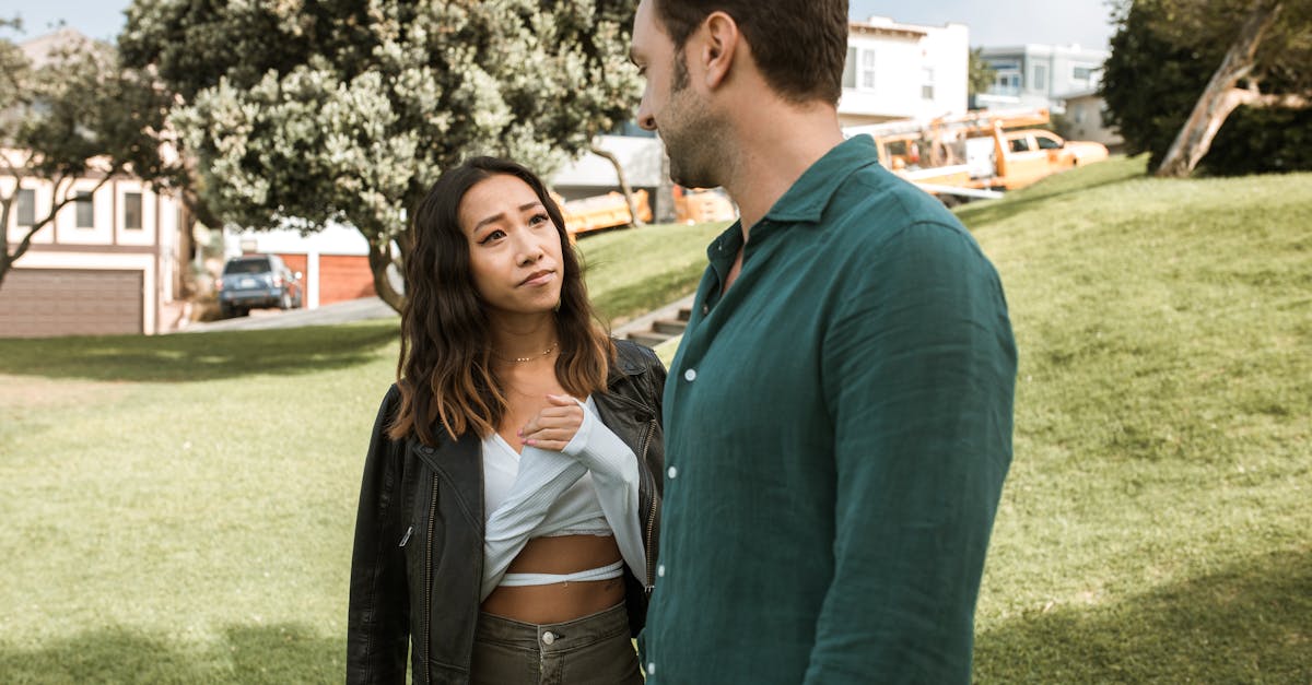 Un homme et une femme conversent en plein air dans un parc ensoleillé entouré d'arbres.