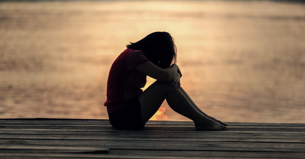 Une femme assise seule sur un quai en bois au bord du lac, incarnant la solitude et la réflexion.