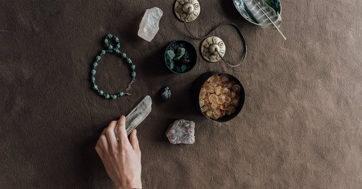 Main disposant des outils spirituels et des cristaux sur une surface en tissu brun naturel.