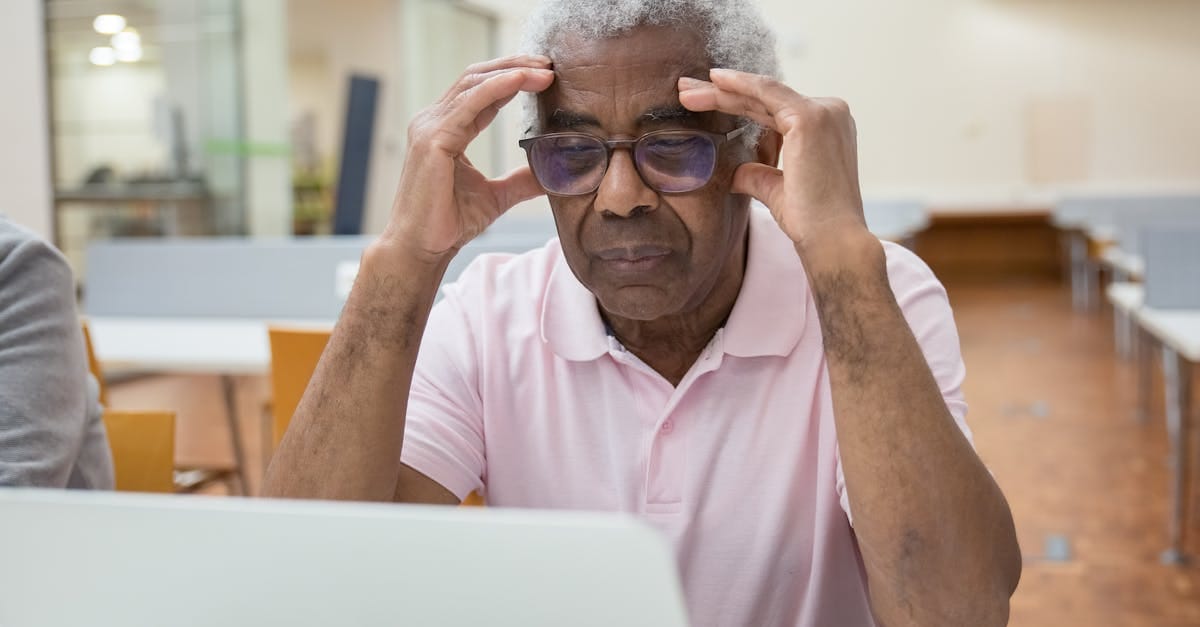 Un homme âgé profondément concentré sur son travail sur ordinateur portable dans un environnement de bibliothèque moderne.