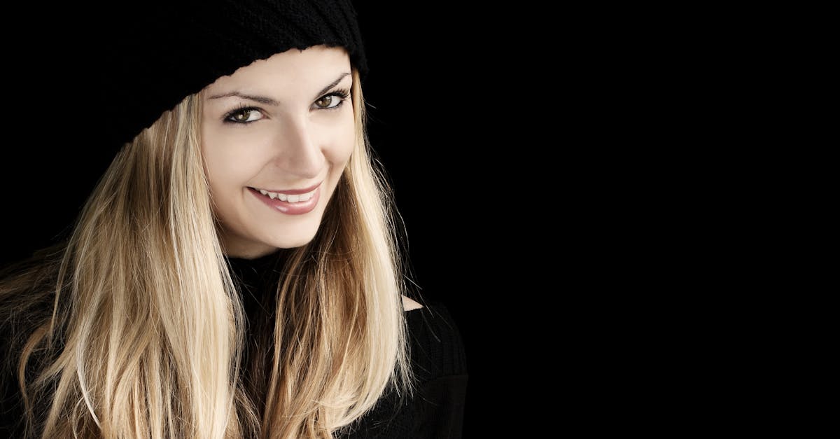 Belle femme aux longs cheveux blonds souriant dans un bonnet noir sur fond sombre